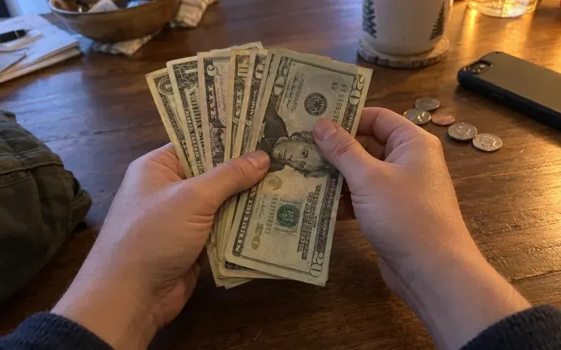 Hands counting a small stack of dollar bills on a table