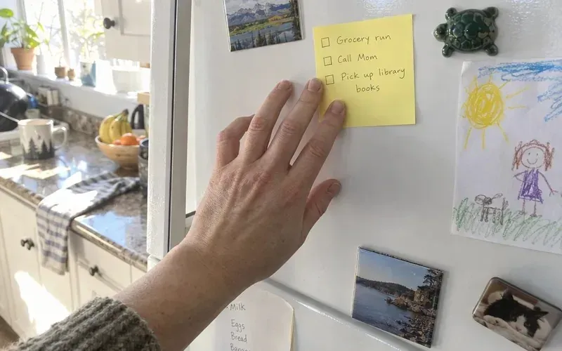 Hand sticking a short handwritten checklist onto a fridge door
