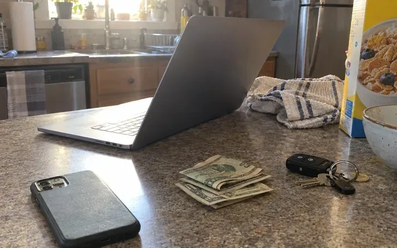 Phone, laptop and a few dollar bills on a kitchen counter