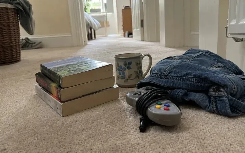 Old game controller, paperback books, a vintage mug and a denim jacket piled up to sell