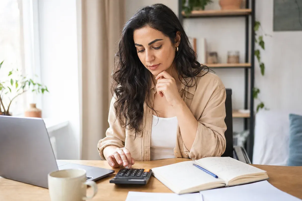 Woman at a desk with a calculator and an open notebook, working out a weekly income goal